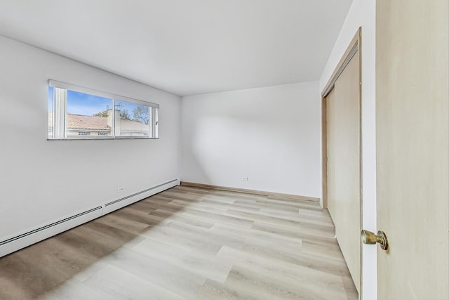 unfurnished bedroom featuring light wood-type flooring, a closet, and baseboard heating