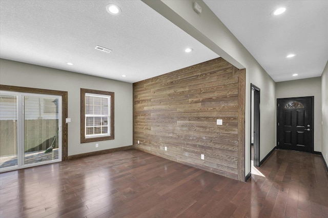 interior space with dark hardwood / wood-style floors, wood walls, and a healthy amount of sunlight