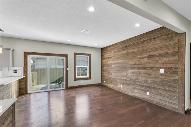 unfurnished living room with a textured ceiling, dark hardwood / wood-style flooring, and wood walls