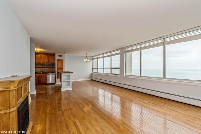 unfurnished living room featuring a water view, light wood-type flooring, baseboard heating, and an inviting chandelier