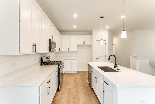 kitchen with a kitchen island with sink, sink, hanging light fixtures, appliances with stainless steel finishes, and white cabinetry