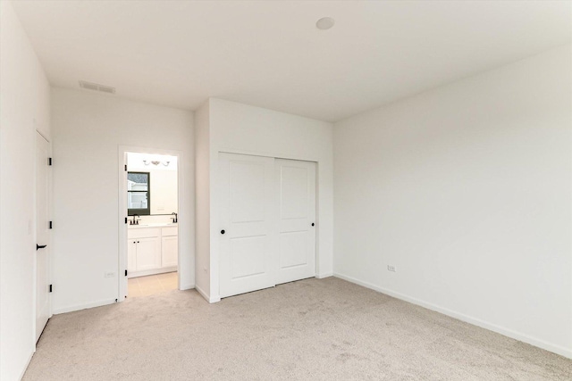 unfurnished bedroom featuring connected bathroom, a closet, and light colored carpet