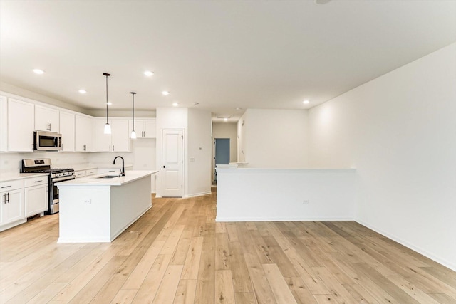 kitchen featuring stainless steel appliances, sink, pendant lighting, white cabinets, and an island with sink