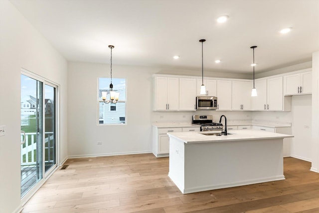 kitchen featuring white cabinets, stainless steel appliances, hanging light fixtures, and an island with sink