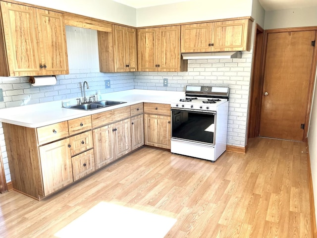 kitchen featuring white gas range, sink, light hardwood / wood-style flooring, range hood, and backsplash