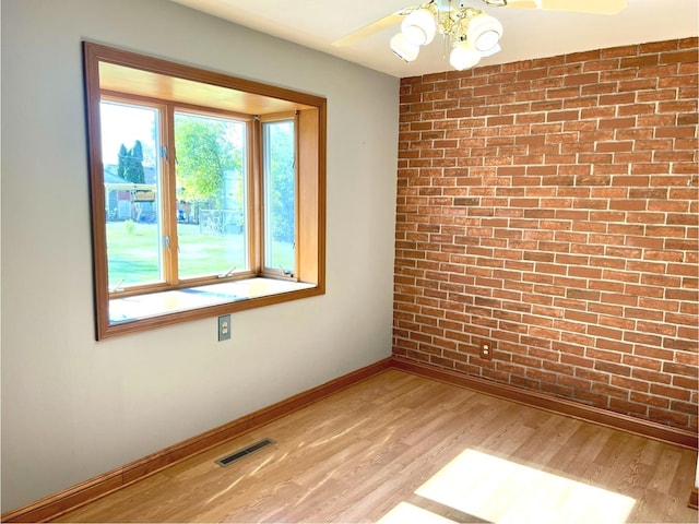 unfurnished room with light hardwood / wood-style floors, ceiling fan, and brick wall