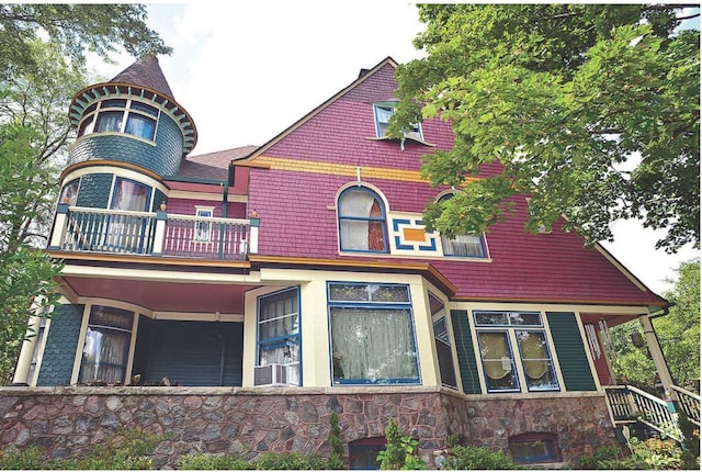 back of house featuring stone siding and a balcony