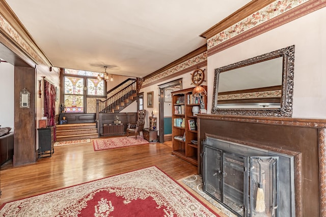 living area with a fireplace with flush hearth, a notable chandelier, wood finished floors, stairs, and crown molding