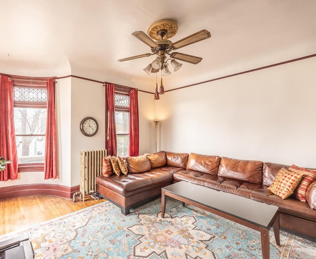 living room featuring radiator heating unit, a ceiling fan, baseboards, and wood finished floors