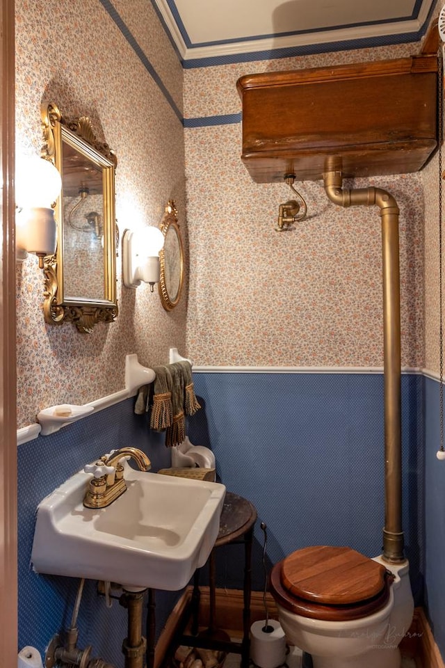 bathroom featuring wallpapered walls, a wainscoted wall, toilet, and a sink