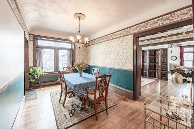 dining area featuring wood-type flooring, wallpapered walls, a textured ceiling, and ceiling fan with notable chandelier