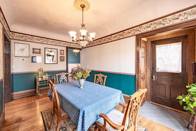 dining area featuring wood finished floors, wainscoting, an inviting chandelier, baseboards, and ornamental molding