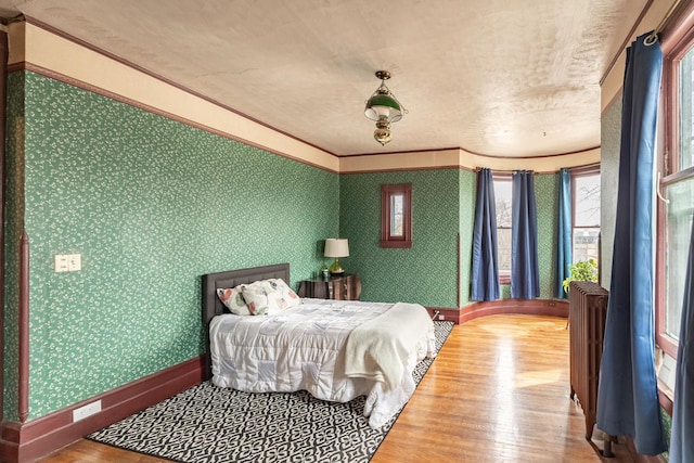 bedroom with radiator heating unit, baseboards, wood finished floors, and multiple windows