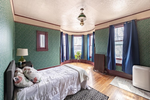 bedroom featuring radiator, multiple windows, wood finished floors, and wallpapered walls