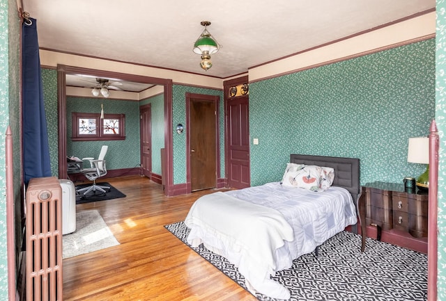 bedroom featuring crown molding, radiator heating unit, wood finished floors, wallpapered walls, and baseboards