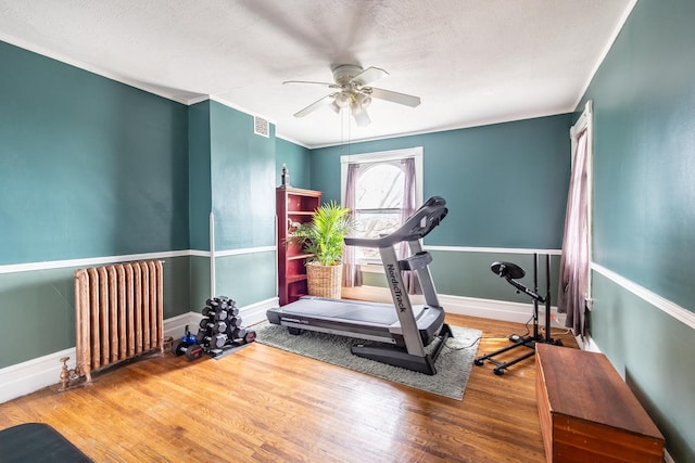 workout area featuring radiator heating unit, wood finished floors, ceiling fan, baseboards, and visible vents