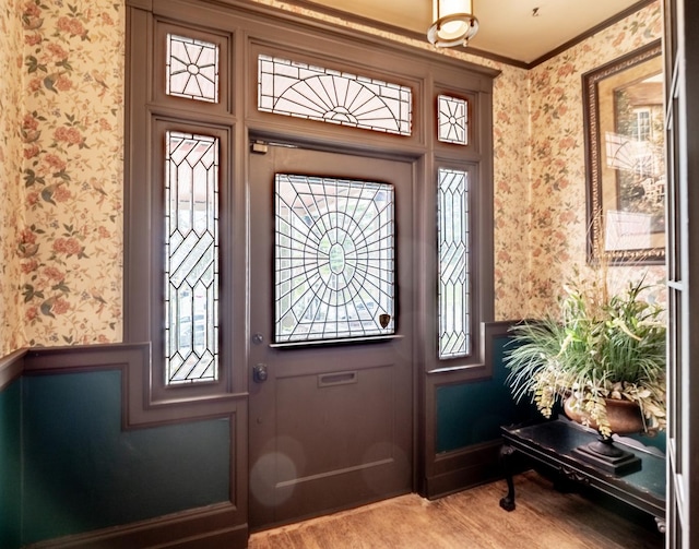 entryway with wallpapered walls, wood finished floors, crown molding, and a wainscoted wall