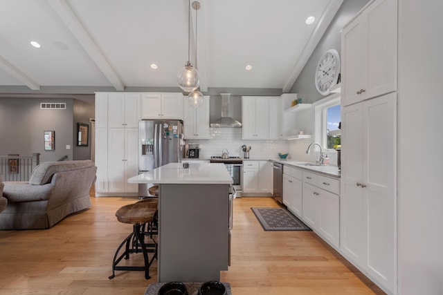 kitchen with a center island, wall chimney exhaust hood, hanging light fixtures, stainless steel appliances, and white cabinets