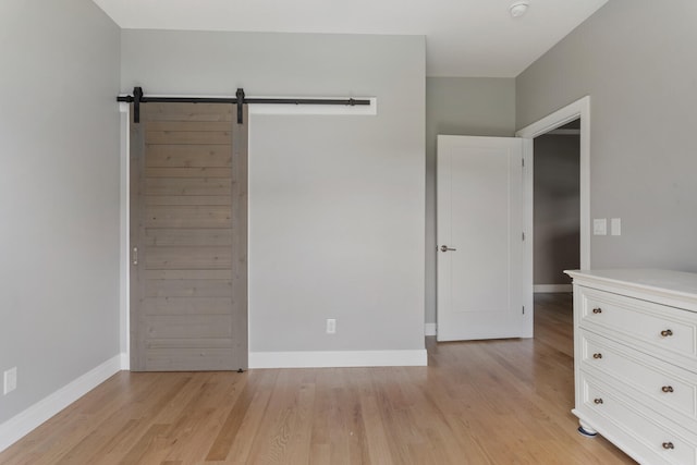 unfurnished bedroom with a barn door and light hardwood / wood-style floors