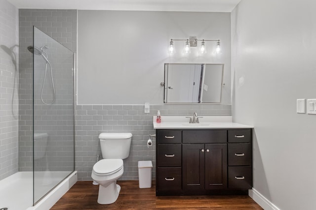 bathroom with hardwood / wood-style floors, toilet, tiled shower, vanity, and tile walls