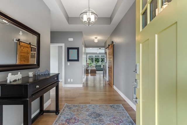 corridor with a barn door, an inviting chandelier, light hardwood / wood-style floors, and a tray ceiling