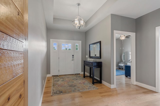 foyer featuring ceiling fan with notable chandelier, light hardwood / wood-style floors, and a raised ceiling