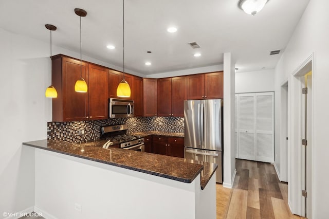 kitchen featuring pendant lighting, dark stone countertops, kitchen peninsula, and stainless steel appliances