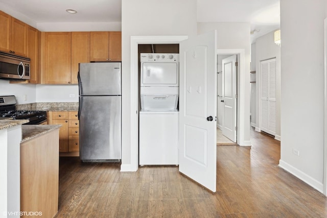 kitchen featuring stainless steel appliances, stacked washer / dryer, light stone countertops, and wood-type flooring