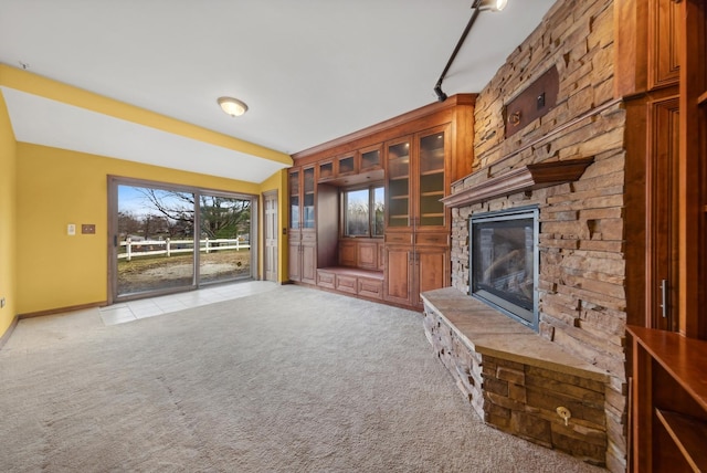 unfurnished living room with lofted ceiling, a stone fireplace, and light colored carpet