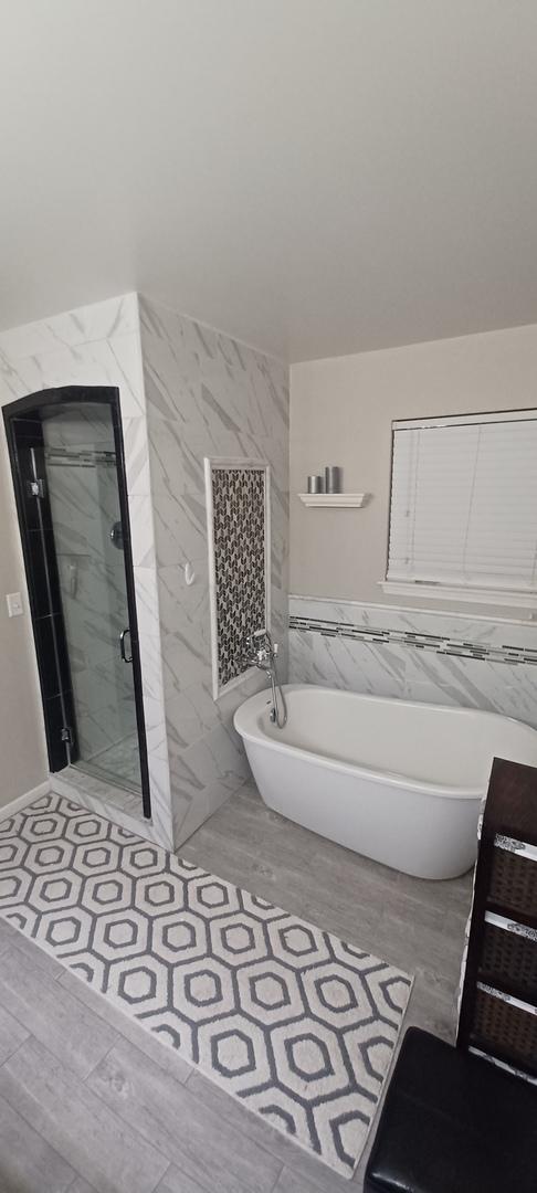 bathroom featuring wood-type flooring, separate shower and tub, and tile walls