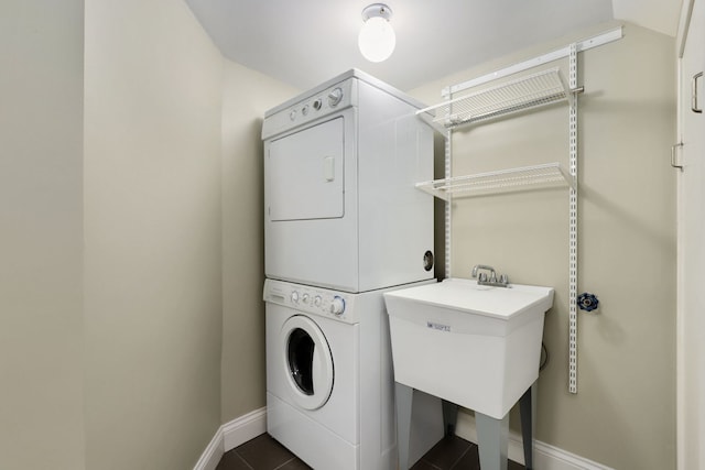 laundry area featuring sink, dark tile patterned floors, and stacked washing maching and dryer