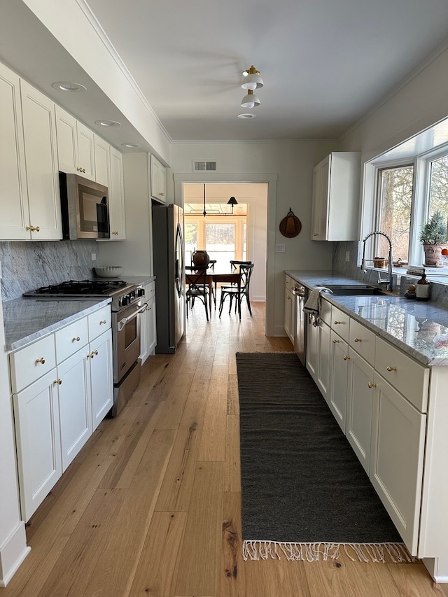 kitchen with white cabinetry, sink, stainless steel appliances, tasteful backsplash, and light stone counters