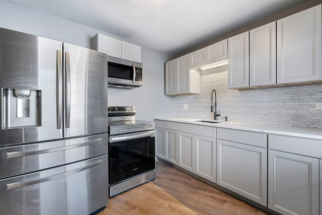 kitchen with sink, stainless steel appliances, gray cabinets, decorative backsplash, and light wood-type flooring