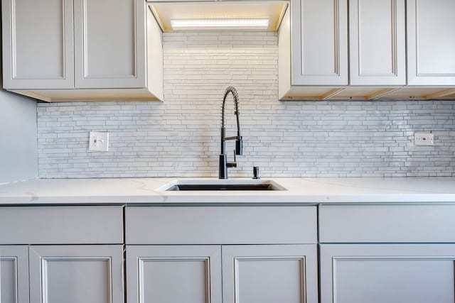 kitchen featuring white cabinets, light stone counters, sink, and tasteful backsplash