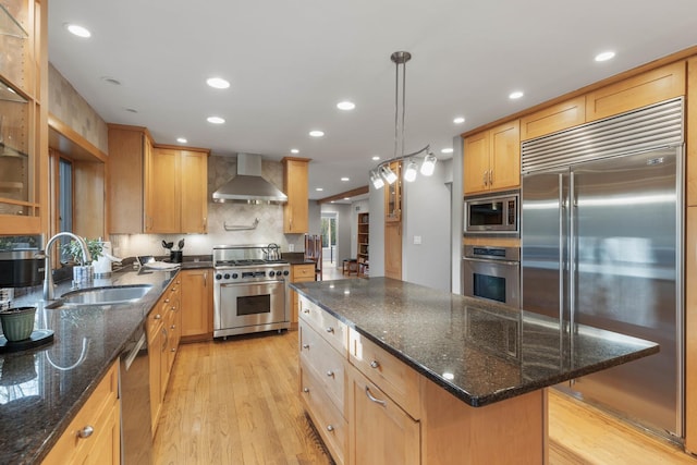 kitchen with sink, hanging light fixtures, wall chimney range hood, built in appliances, and a kitchen island