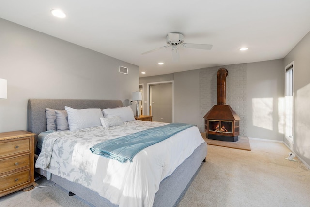 bedroom featuring light colored carpet, a wood stove, and ceiling fan