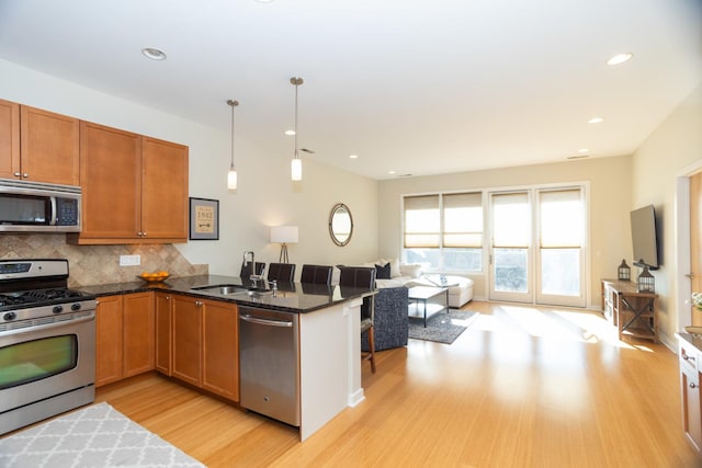 kitchen with sink, stainless steel appliances, backsplash, dark stone counters, and pendant lighting