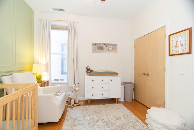 bedroom featuring a crib, light wood-type flooring, and multiple windows