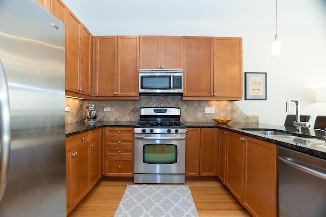 kitchen with sink, hanging light fixtures, dark stone countertops, light hardwood / wood-style floors, and stainless steel appliances