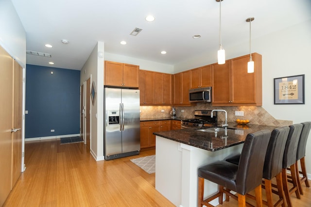 kitchen featuring stainless steel appliances, kitchen peninsula, dark stone countertops, pendant lighting, and a breakfast bar