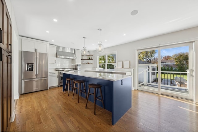 kitchen featuring wall chimney exhaust hood, white cabinets, decorative light fixtures, a kitchen island, and high end appliances