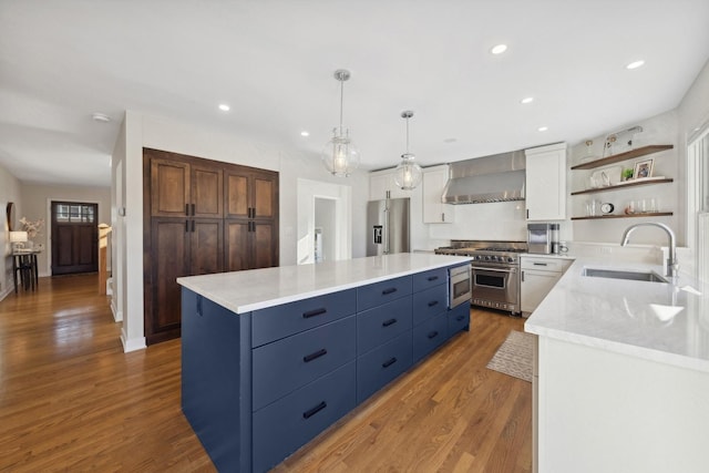 kitchen with a kitchen island, high end appliances, sink, wall chimney range hood, and white cabinetry