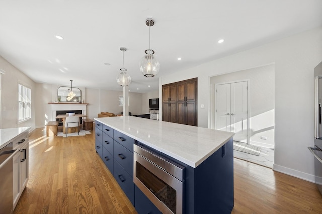 kitchen featuring light stone countertops, stainless steel appliances, decorative light fixtures, a center island, and light hardwood / wood-style floors