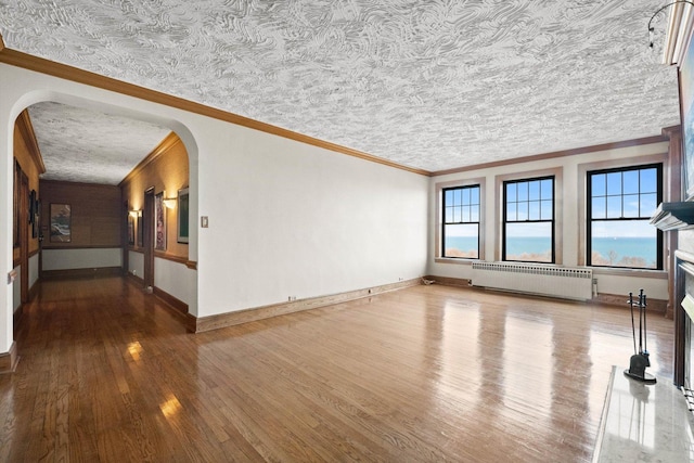 unfurnished room featuring radiator heating unit, plenty of natural light, ornamental molding, and wood-type flooring