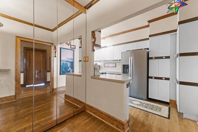 kitchen featuring kitchen peninsula, stainless steel fridge, light hardwood / wood-style floors, white cabinetry, and hanging light fixtures