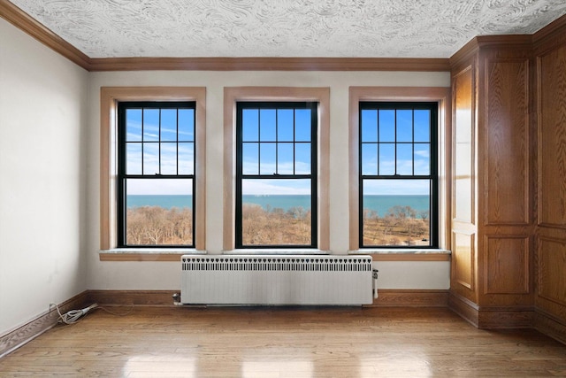 spare room featuring crown molding, radiator heating unit, a textured ceiling, and light wood-type flooring