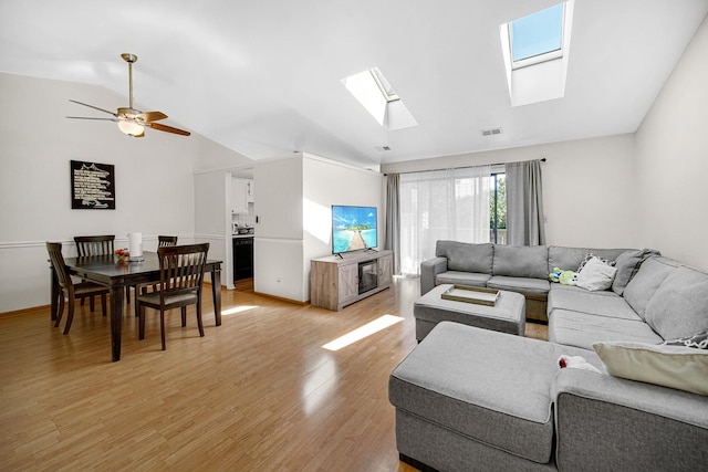 living room featuring ceiling fan, light wood-type flooring, and lofted ceiling with skylight