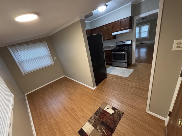 kitchen with black fridge, stainless steel gas range oven, dark brown cabinetry, crown molding, and light hardwood / wood-style floors