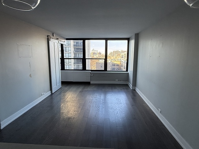 unfurnished room with a barn door and dark wood-type flooring