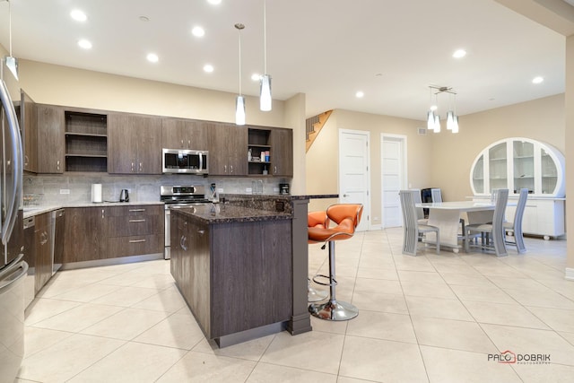 kitchen featuring a kitchen island with sink, hanging light fixtures, decorative backsplash, dark brown cabinetry, and stainless steel appliances